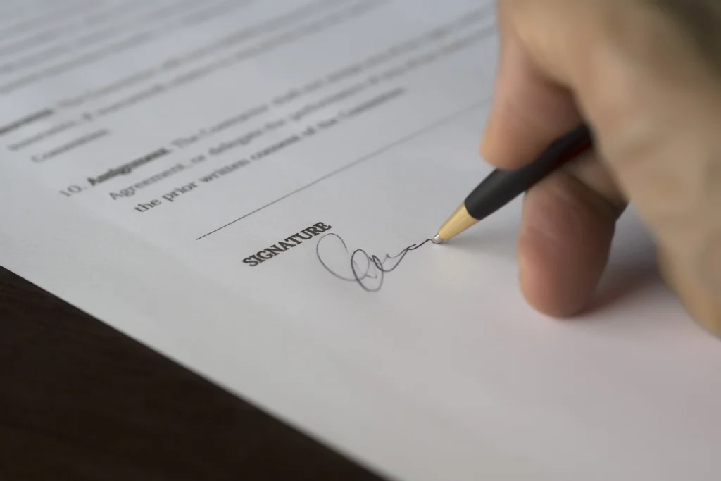 Hand unterschreibt mit einem Stift ein Vollmachtsdokument, Fokus auf die Unterschriftenzeile mit dem Label "SIGNATURE".