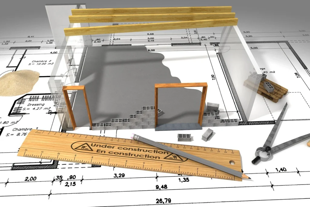 Architekturmodell auf Blaupausen mit Holzbalken, Werkzeugen, Lineal mit der Aufschrift "Im Bau", Sand und Ziegelsteinen, das die Einhaltung der Baunormen zeigt.