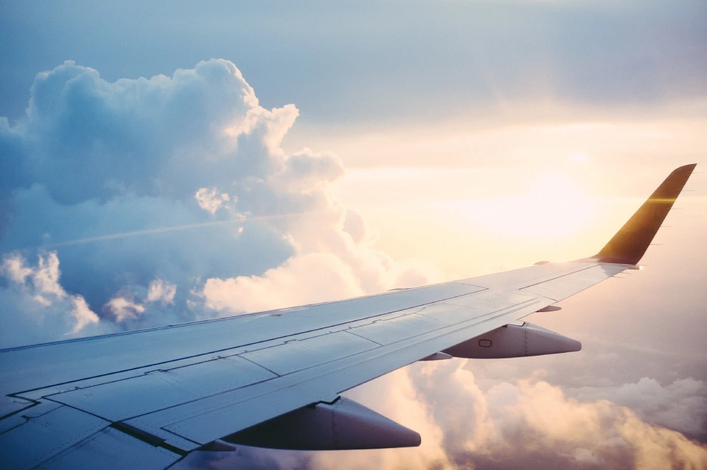 Blick aus einem Flugzeugfenster: Flugzeugflügel über den Wolken, die Sonne scheint hell und schafft einen traumhaften Himmel - ideal für Reiseberichte.