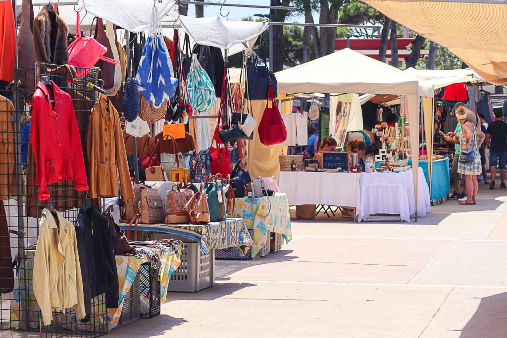 Markt im Freien mit bunten Ständen, die Jacken, Taschen und Kunsthandwerk verkaufen. An einem sonnigen Tag stöbern die Käufer unter Zelten.