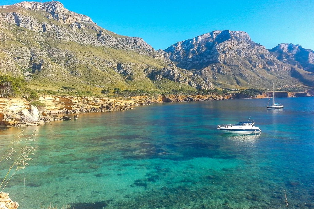 Boote ankern im klaren türkisfarbenen Wasser bei Betlem, mit grünen Bergen und einem strahlend blauen Himmel im Hintergrund.
