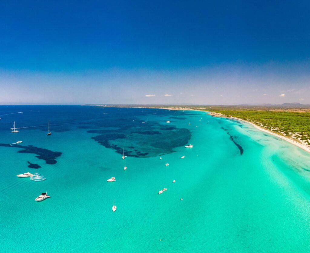 Luftaufnahme des Strandes von Mallorca: türkisfarbenes Wasser, Boote, üppige grüne Landschaft und klarer Himmel - ein wunderschöner Strand der Insel.