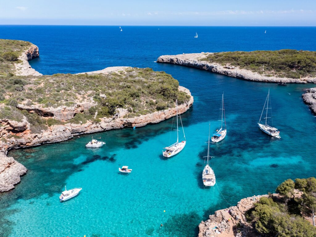 Türkisfarbene Bucht mit felsigen Klippen, grünen Pflanzen, verankerten Segelbooten - Mallorcas schönster Strand in der Sonne.