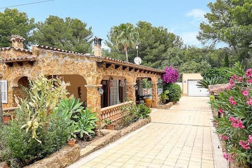 Charmantes Steinhaus mit gewölbter Veranda, üppigem Garten, Einfahrt, kleiner Garage, hohen Bäumen und strahlend blauem Himmel auf Mallorca.